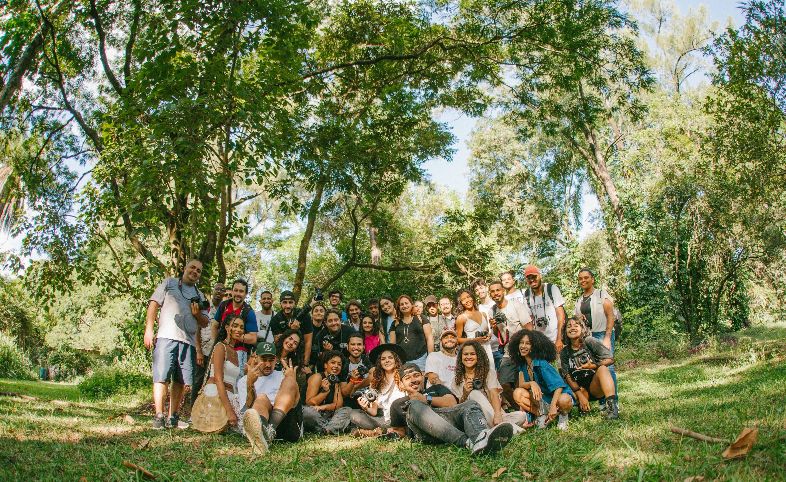 A diverse group of joyful people posing together outdoors in a sunny park setting.